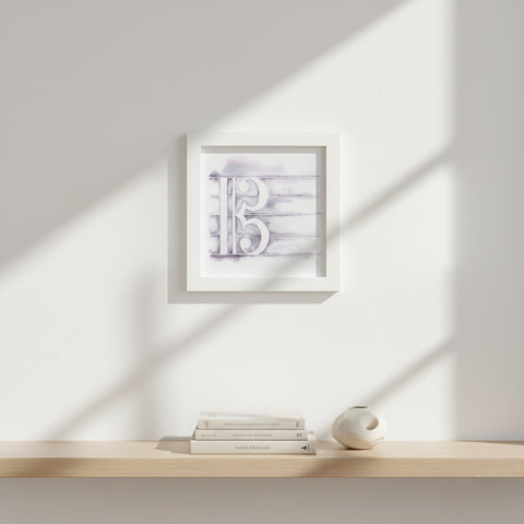 Framed artwork on a shelf with books and a candle against a light wall.