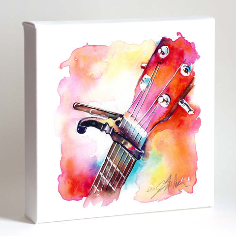 A vibrant watercolor painting of a guitar headstock with a capo, featuring bright pink-coral hues and other colors, displayed in a white frame.