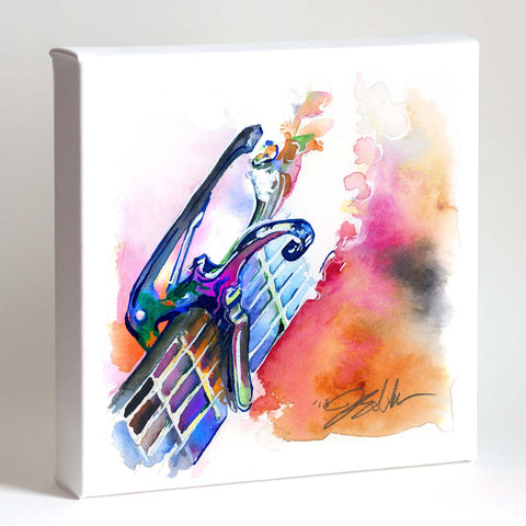 A vibrant watercolor painting of a guitar capo and headstock displayed in a white frame, with abstract splashes of blue, pink, and orange.
