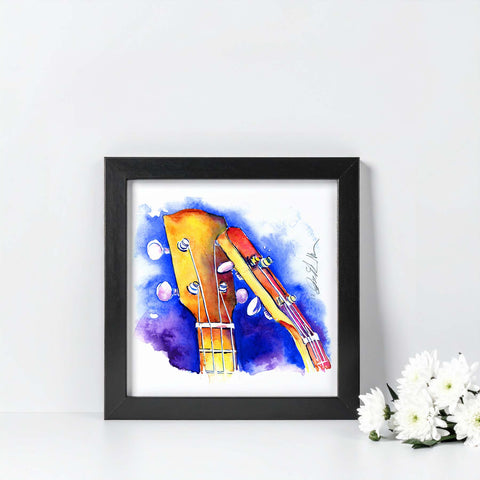 Framed artwork of a colorful uke headstock on a white wall with flowers.
