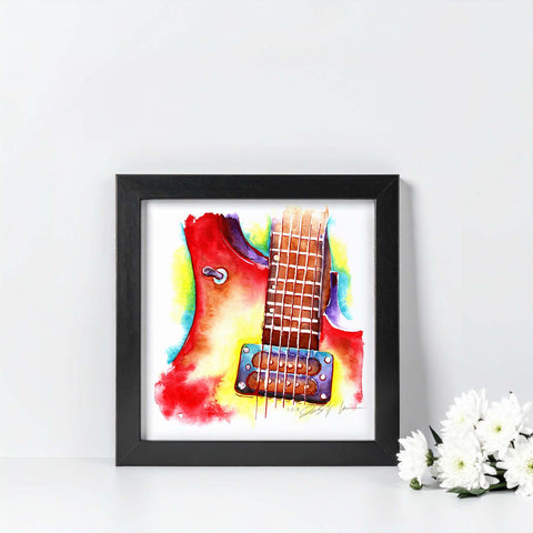 Framed artwork of a colorful guitar on a white surface with flowers.