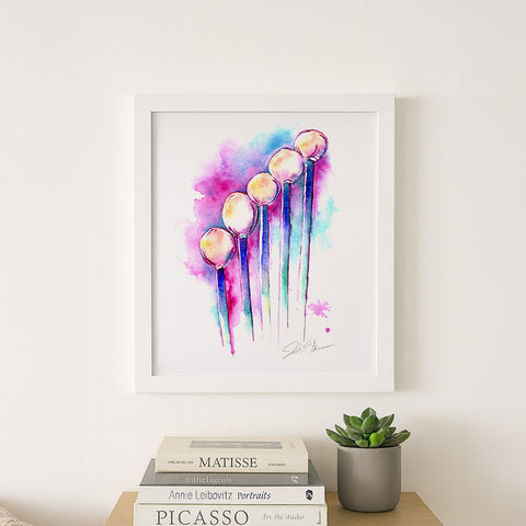 Framed colorful abstract art print on a wall above books and a plant.