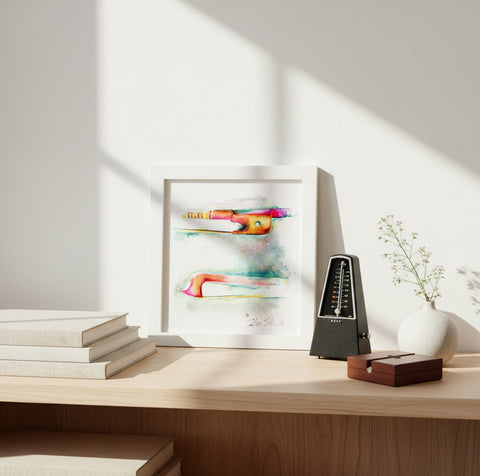 Framed watercolor artwork on a wooden surface with a metronome and books.