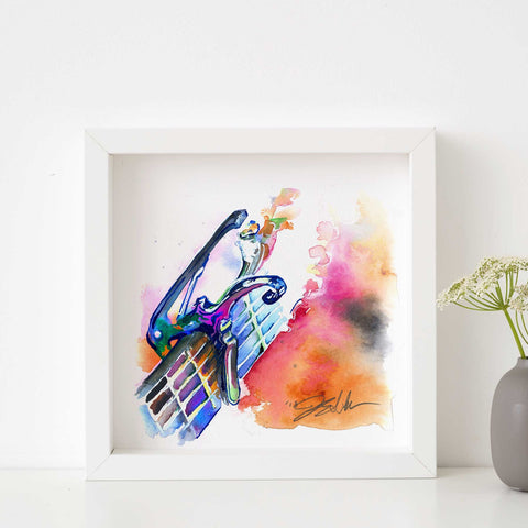 A vibrant watercolor painting of a guitar capo and headstock displayed in a white frame, with abstract splashes of blue, pink, and orange.